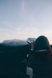 Rear view of woman looking through binoculars during sunset