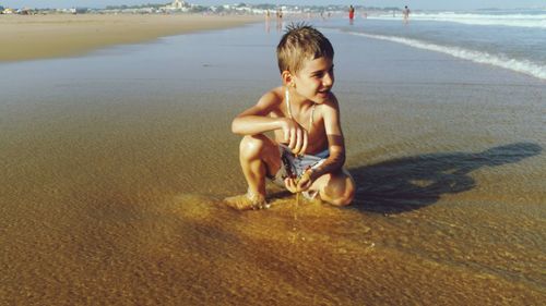 Shirtless boy kneeling on shore at beach
