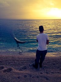 Rear view of man pulling fishing net from sea during sunset