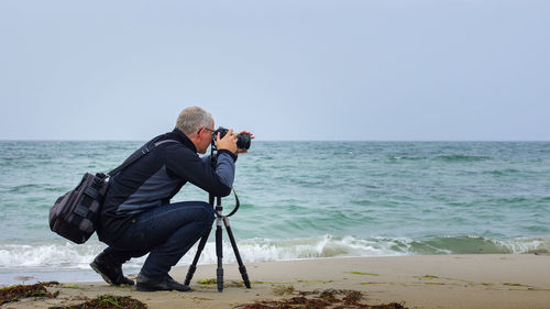 Man photographing at beach against clear sky