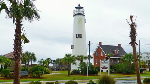 Lighthouse amidst trees and buildings against sky