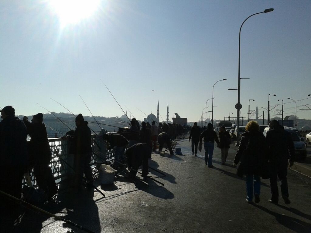 men, large group of people, lifestyles, sunlight, person, sun, clear sky, leisure activity, sky, street light, medium group of people, mixed age range, sunbeam, walking, transportation, sunny, silhouette, street, lens flare