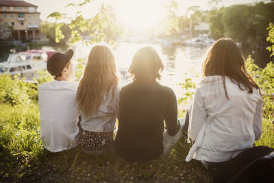 Rear view of teenagers sitting at lakeshore