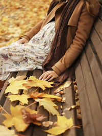 Midsection of woman sitting on wood during autumn