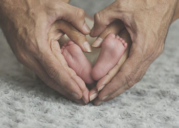 Cropped hands of parents forming heart shape around baby feet