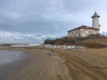 Lighthouse on beach by sea against sky