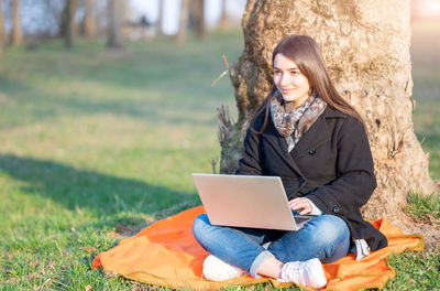 Young woman using laptop while sitting on field