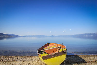 Boat moored at lakeshore against clear blue sky
