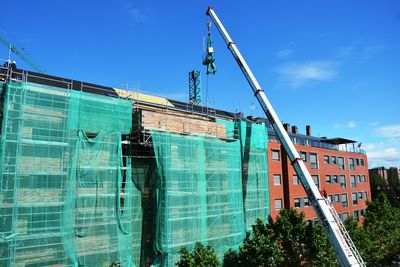 Low angle view of crane by building against blue sky