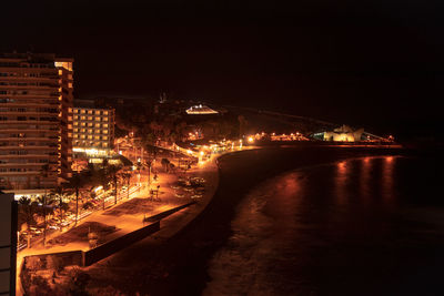 Illuminated buildings by river against sky in city at night