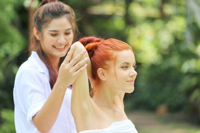 Smiling woman helping friend in practicing yoga in park