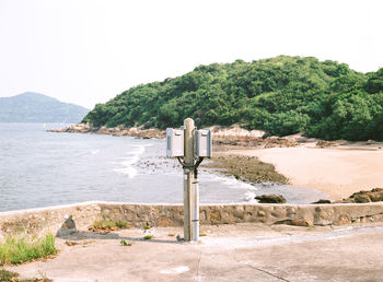 Electric meter boxes on pole by sea against clear sky