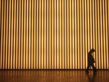 Silhouette man walking against illuminated pattern wall at night