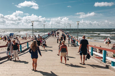 Group of people on boardwalk at beach against sky