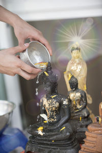 Cropped hand pouring water over buddha statue