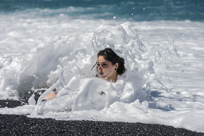 Surf splashing on young woman on shore at beach