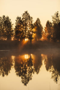 Silhouette trees by lake against sky during sunset