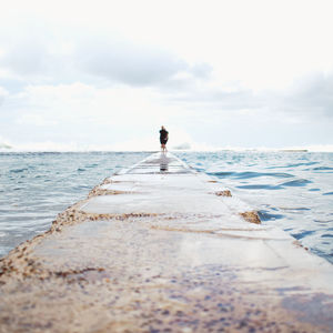 Rear view of woman walking on beach against sky