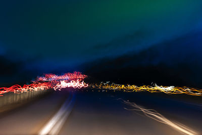 Light trails on road by illuminated city against sky at night