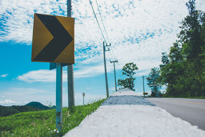 Road sign by trees against sky