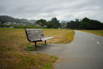 Empty bench by road against sky