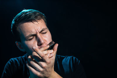 Man playing harmonica against black background