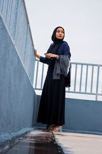 Portrait of young woman standing against railing