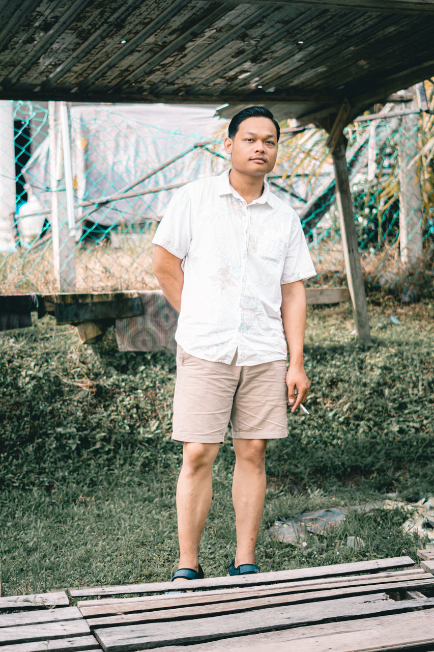 one person, standing, adult, full length, front view, men, casual clothing, day, portrait, smiling, lifestyles, spring, leisure activity, shorts, young adult, looking at camera, nature, happiness, emotion, architecture, outdoors, person, clothing, plant, built structure