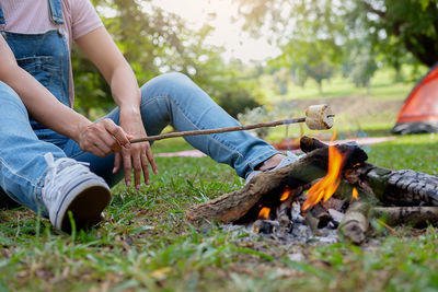 Low section of woman roasting marshmallow on campfire