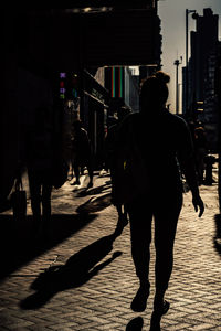 Rear view of people walking on sidewalk in city