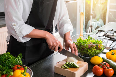 Midsection of chef cutting vegetables in kitchen