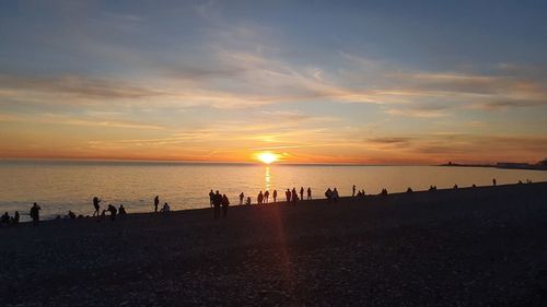 Silhouette people on beach against sky during sunset