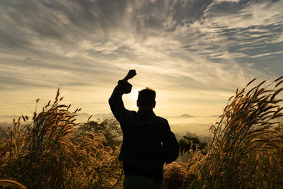 Silhouette man clenching fist on field against sky during sunset