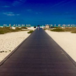 Boardwalk on beach against blue sky