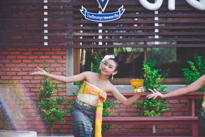 Full length of woman holding umbrella against brick wall