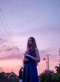 Side view of young woman standing against sky during sunset