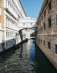 Canal amidst buildings against blue sky in city during sunny day