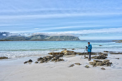 Man on rocks at beach against sky