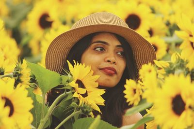 Beautiful young woman wearing hat by yellow flowers