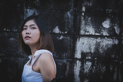 Portrait of woman looking away while standing against wall