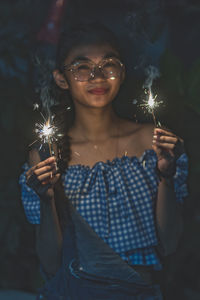 Portrait of young woman holding sparklers at night
