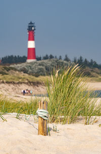 Lighthouse on field by building against sky