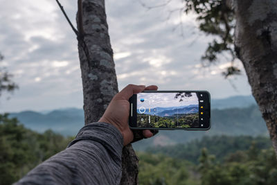 Midsection of person photographing camera on mobile phone against sky