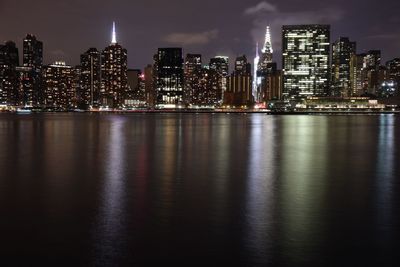 Illuminated buildings by river against sky at night