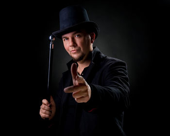 Portrait of mature man wearing hat while standing against black background