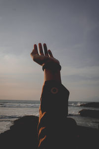 Human hand on sea shore against sky