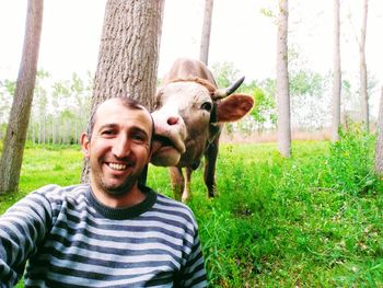 Portrait of smiling man with cow standing by tree trunk