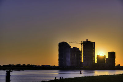 Silhouette buildings by lake against sky during sunset