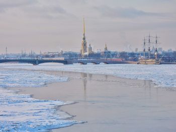 View of buildings by frozen river against cloudy sky