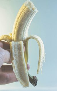 Cropped hand holding banana against sky